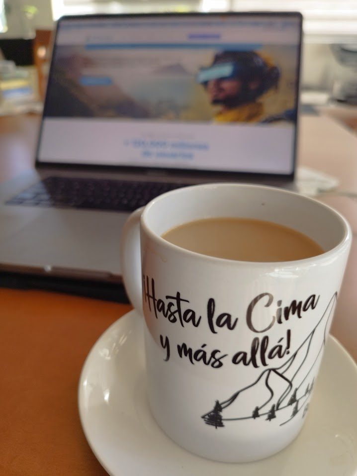 Taza con el lema Hasta la cima y más allá frente a un escritorio de trabajo